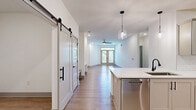 Located at 3 Whisperwood Way in Candler, NC, this single-story home offers a thoughtfully designed open-concept layout with clean, modern finishes throughout. Light hardwood-style flooring flows through the main living areas, complemented by crisp white walls and contemporary gray baseboards that give the home a fresh, cohesive aesthetic.

The kitchen is a standout feature, equipped with gray shaker-style cabinetry, white quartz countertops, stainless steel appliances including a French door refrigerator and built-in microwave, and a peninsula with pendant lighting overhead. A stylish barn door connects the kitchen area to the adjacent living space, adding architectural character. The dining room is conveniently positioned nearby for seamless entertaining.

The spacious primary bedroom is carpeted for comfort and includes a ceiling fan, with direct access to the shared bathroom. The bathroom features a dual-sink vanity with white quartz countertops, gray cabinetry, matte black fixtures, and a large framed mirror with modern sconce lighting. A walk-in closet with wire shelving provides ample storage.

The second bedroom is also carpeted and well-sized. A dedicated laundry room with full-size washer and dryer adds everyday convenience. The home presents a clean, move-in ready interior with modern design details throughout.