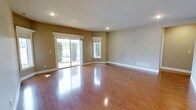 This single-story home offers a well-designed layout with three bedrooms and two bathrooms, providing ample space for comfortable living. The main living area is immediately welcoming, featuring gleaming hardwood floors that reflect natural light pouring in through a sliding glass door and an adjacent window framed with clean white molding. Neutral, warm-toned walls complement the flooring throughout, creating a cohesive and inviting atmosphere. Recessed lighting adds a modern touch while ensuring consistent illumination across the open space.

The floor plan, as seen in the layout overview, arranges the three bedrooms along the left and lower wings of the home, each benefiting from the same rich hardwood flooring found throughout. The two bathrooms are conveniently positioned to serve both the bedrooms and the main living spaces. White baseboards and trim provide clean architectural contrast against the warm wall tones in every room.

The sliding glass door in the living area opens to an outdoor view, enhancing the sense of openness and allowing for excellent natural light. Floor vents are strategically placed for efficient climate control. Overall, this home presents a clean, move-in-ready aesthetic with consistent finishes and a practical, flowing single-floor design.