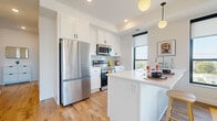This contemporary single-floor residence is designed with a clean, modern aesthetic defined by white walls, light hardwood-style flooring, and large windows that invite abundant natural light. The open-concept kitchen is a standout feature, outfitted with crisp white shaker cabinetry, a subway tile backsplash, stainless steel appliances—including a French door refrigerator, electric range, and microwave—and a peninsula with a white quartz countertop that provides seating and additional prep space. Globe pendant lighting adds a refined finishing touch overhead. Adjacent to the kitchen, the living area is bright and welcoming, anchored by a large sliding glass door that opens onto a private balcony with open outdoor views. The bedroom is a calm retreat, featuring plush carpet, a large window with exterior views, and direct access to a spacious walk-in closet equipped with wire shelving for organized storage. The bathroom is clean and functional, offering a full tub-shower combination with white tile surround and wood-look flooring. Throughout the residence, consistent finishes and thoughtful design details create a cohesive, move-in-ready living environment.
