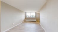 Located on the third floor at 552 Birchmount Rd in Toronto's Scarborough district, this one-bedroom, one-bathroom unit offers a clean, functional layout across a single floor. Light-toned hardwood flooring runs throughout the living and sleeping areas, creating a bright and cohesive aesthetic complemented by neutral warm-beige walls and crisp white baseboards.

The open living room is a comfortable and well-lit space, anchored by a large picture window that frames outdoor views and allows generous natural light to fill the room. A baseboard heating unit runs beneath the window, providing efficient warmth. The space flows naturally toward the rest of the unit, maintaining an easy sense of continuity.

The galley-style kitchen features white cabinetry along both walls, offering ample storage. It is equipped with stainless steel appliances including a refrigerator and electric range, with granite-style countertops and light ceramic tile flooring underfoot. Overhead lighting ensures the kitchen is well-illuminated throughout.

The bedroom is a well-proportioned private retreat with its own window overlooking the surroundings, continuing the light hardwood floors and neutral palette. A built-in closet with sliding doors provides practical storage.

The bathroom is finished with classic white wall tiles surrounding a full bathtub and shower combination, complemented by a mosaic tile floor with warm brown accents, a toilet, and a sink — offering a tidy, functional space.