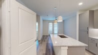 This thoughtfully designed 1-bedroom, 1-bathroom unit offers a clean, modern aesthetic across its single floor. The open-concept kitchen serves as the centerpiece, featuring a large granite-topped island with an undermount sink, elegant pendant lighting, gray shaker-style cabinetry, a decorative tile backsplash, and a full suite of stainless steel appliances including a refrigerator with ice maker, range, and microwave. Wood-look flooring flows through the kitchen and living areas, creating a warm, cohesive feel. The bedroom is a comfortable, carpeted retreat bathed in a neutral palette, offering direct access to the bathroom and a dedicated walk-in closet equipped with built-in shelving and a hanging rod for ample storage. The bathroom is finished with granite countertops, a white vanity with modern hardware, wood-look tile flooring, and a tub-shower combination accented by full-height stone-look tile surround. A door from the living area provides access to a small outdoor area, allowing natural light to filter into the space. Throughout the unit, crisp white trim, neutral wall tones, and contemporary fixtures contribute to a clean, move-in-ready environment.