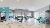 Located at 2759 Towne Blvd in Middletown, Ohio, this single-floor community amenity space offers a well-appointed, open-concept layout designed for gathering, socializing, and productivity. The interior is finished with striking marble-patterned tile flooring that flows throughout, complemented by a fresh color palette of cool grays and vibrant teal accent walls that give the space a modern, energetic character.

Vaulted ceilings with large ceiling fans enhance the sense of spaciousness, while recessed lighting ensures the room is well-lit throughout. Multiple round dining tables paired with teal shell chairs provide ample communal seating, making the space ideal for casual gatherings. A dedicated lounge area features patterned accent chairs and a glass side table, offering a quieter setting for conversation or relaxation.

A built-in workstation area along one wall includes dark wood cabinetry and individual desk stations with task chairs, catering to residents seeking a productive work environment. Storage is accessible via double interior doors with classic panel detailing.

Floor-to-ceiling windows along two walls flood the space with natural light and provide unobstructed views of the outdoor pool courtyard and surrounding community. A glass-paneled entry door with sidelights creates a welcoming, light-filled entrance. The overall ambiance is contemporary and inviting, balancing function with vibrant, thoughtful design.