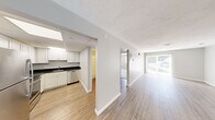 This single-floor residence offers a clean, modern interior highlighted by light hardwood-style flooring that flows throughout the main living areas. The open-concept layout connects a spacious living room — filled with natural light through a large sliding glass door — to the kitchen and adjacent spaces, creating an easy sense of flow and openness.

The kitchen is thoughtfully updated with crisp white shaker cabinetry, dark granite countertops, and a full suite of stainless steel appliances, including a range, over-the-range microwave, and dishwasher. A skylight overhead adds a bright, airy quality to the space.

The bedrooms feature soft wall-to-wall carpeting and neutral tones, with windows fitted with horizontal blinds that allow for natural light and privacy control. Each bedroom includes closet storage, with at least one room offering a reach-in closet with a hanging rod.

The bathroom is efficiently designed, featuring a tub-shower combination with built-in shelving, a white vanity with dark countertop, and overhead cabinetry for additional storage. Hardwood-style flooring extends into the bathroom, maintaining a consistent aesthetic.

Throughout the unit, white trim, neutral wall colors, and recessed and flush-mount lighting contribute to a bright, clean, and move-in-ready atmosphere.