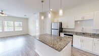 This contemporary 1170 square foot apartment in Jacksonville, FL offers a blend of comfort and style. The single-story layout includes three bedrooms, with the primary bedroom spanning a generous 170 square feet. The open-concept design seamlessly integrates the kitchen and living areas, creating a spacious feel.

The kitchen is a highlight, boasting sleek white cabinetry, stainless steel appliances, and an attractive granite countertop island. Modern pendant lighting adds a touch of elegance. Throughout the apartment, wood-look flooring creates a warm, inviting atmosphere, while large windows flood the rooms with natural light.

The bathrooms feature granite countertops and are equipped with safety grab bars, indicating attention to accessibility. Ample closet space, including a walk-in closet with adjustable shelving, provides plenty of storage options.

The apartment's exterior showcases a welcoming front porch with white railings, overlooking a well-maintained parking area. The surrounding landscape includes manicured lawns and young trees, suggesting a pleasant, community-oriented environment.

With its combination of modern amenities, thoughtful design, and convenient location, this apartment offers an attractive living solution for those seeking a contemporary home in Jacksonville.