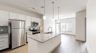 Located at 601 Avenida Cesar E Chavez in Kansas City, MO, this well-appointed one-bedroom, one-bathroom unit offers a thoughtfully designed open-concept layout across a single floor. The combined living, dining, and kitchen area serves as the heart of the home, showcasing warm wood-look flooring, crisp white cabinetry, a subway tile backsplash, and a large granite-topped kitchen island with an undermount sink and pendant lighting overhead. Stainless steel appliances, including a refrigerator, range, and microwave, complete the modern kitchen. Large windows allow natural light to fill the living area, which opens to a private balcony. The carpeted bedroom offers a comfortable retreat with a window fitted with blinds for light control and two closets, including a spacious walk-in with wire shelving. The bathroom features a granite-topped vanity with ample drawer storage, wood-look flooring, and direct access to the walk-in closet. Additional conveniences include a dedicated laundry area and a utility room. The unit's clean, neutral palette and contemporary finishes create a bright, cohesive ambiance throughout.