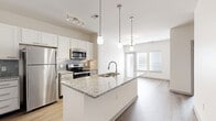 Located at 601 Avenida Cesar E Chavez in Kansas City, MO, this well-appointed one-bedroom, one-bathroom unit offers a thoughtfully designed open-concept layout across a single floor. The combined living, dining, and kitchen area serves as the heart of the home, showcasing warm wood-look flooring, crisp white cabinetry, a subway tile backsplash, and a large granite-topped kitchen island with an undermount sink and pendant lighting overhead. Stainless steel appliances, including a refrigerator, range, and microwave, complete the modern kitchen. Large windows allow natural light to fill the living area, which opens to a private balcony. The carpeted bedroom offers a comfortable retreat with a window fitted with blinds for light control and two closets, including a spacious walk-in with wire shelving. The bathroom features a granite-topped vanity with ample drawer storage, wood-look flooring, and direct access to the walk-in closet. Additional conveniences include a dedicated laundry area and a utility room. The unit's clean, neutral palette and contemporary finishes create a bright, cohesive ambiance throughout.