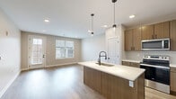 Located at 196 Westfield Rd in Noblesville, Indiana, this thoughtfully designed one-bedroom, one-bathroom residence offers a comfortable and modern living experience across a single floor. The open-concept kitchen and living area serves as the heart of the home, featuring rich wood-tone cabinetry, white quartz countertops, a central island with pendant lighting, subway tile backsplash, and a full suite of stainless steel appliances. Warm-toned hardwood-style flooring flows seamlessly throughout the main living areas, lending a cohesive and inviting aesthetic. The living room is bright and airy, with recessed lighting, neutral walls, and access to an outdoor area through a glass-paneled door framed by large windows that welcome natural light. The spacious bedroom is finished with plush carpeting, a ceiling fan, and generous windows with views of the surrounding neighborhood. A dedicated closet provides convenient storage. The bathroom is elegantly appointed with a glass-enclosed walk-in shower clad in large-format light gray tile, matte black hardware accents, and hardwood-style flooring. Two hallways connect the spaces efficiently, contributing to a smooth and functional floor plan throughout this well-crafted residence.