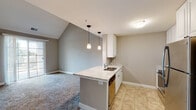 This two-story residence is designed with an open-concept layout on the main level, where the kitchen and living area flow seamlessly together. The kitchen is equipped with stainless steel appliances, including a refrigerator, range, and over-the-range microwave, complemented by white cabinetry, granite-style countertops, and a peninsula with an undermount sink. Pendant lighting hangs above the peninsula, adding a functional and decorative element. Tile flooring extends through the kitchen, while the adjacent living area features plush carpet and a sliding glass door that opens to an outdoor balcony, allowing natural light to fill the space. Vaulted ceilings on this level contribute to an open, airy atmosphere.

The upper level includes multiple carpeted bedrooms, each with ceiling fans and ample natural light from well-placed windows. A open loft-style hallway with a railed overlook connects the upper rooms. The bathrooms are finished with granite-topped vanities, white cabinetry, and tile flooring. The primary bathroom features a tub-shower combination and an extended vanity, while a secondary bathroom offers a similarly clean, neutral aesthetic throughout.