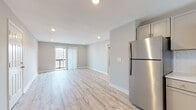 This single-floor space presents a clean, contemporary design highlighted by light-toned luxury vinyl plank flooring that runs consistently throughout. The open-concept living area is bright and spacious, with recessed lighting overhead and a sliding glass door that opens to a private balcony, allowing natural light to fill the room and providing outdoor views.

The kitchen is thoughtfully laid out in an L-shaped configuration, featuring gray shaker-style cabinetry, white countertops, a subway tile backsplash, and a full suite of stainless steel appliances including a refrigerator, range, over-the-range microwave, and dishwasher. A window above the sink further brightens the space.

Two well-proportioned bedrooms each feature light gray walls, light wood-tone flooring, and ceiling fans with integrated lighting. Each room is equipped with multiple windows fitted with horizontal blinds, ensuring ample natural light and ventilation.

The bathroom features a neutral palette with white hexagonal tile flooring, marble-look wall tile in the shower area, a gray vanity with a white basin, and elegant gold-toned fixtures and hardware. An entry area near the front door provides additional closet access, completing this well-organized and move-in-ready layout.