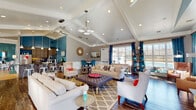 Located at 44760 Locust Ridge Ct in California, Maryland, this single-floor space combines striking architectural details with a warm, inviting atmosphere. The main living area commands immediate attention with its soaring vaulted ceiling accented by decorative beams and a teal-painted peak, complemented by an array of recessed lighting and a stylish pendant chandelier. Rich hardwood flooring flows throughout, grounding the space with a sense of warmth.

A floor-to-ceiling stacked stone fireplace serves as a dramatic focal point, topped by a mounted flat-screen television and flanked by large windows dressed in bold teal drapery that allow generous natural light to fill the room. The seating area is generously proportioned, accommodating multiple lounge groupings arranged around a tufted ottoman coffee table atop a geometric patterned area rug.

The open kitchen features natural wood cabinetry, dark granite countertops, stainless steel appliances including double wall ovens and a refrigerator, and a large island with bar seating for several guests. Pendant lighting in brushed nickel adds a modern touch against the vivid teal accent wall.

A separate dining nook offers bistro-style high-top seating beneath crown molding and wainscoting. The overall design blends contemporary and transitional styles with a cohesive, energetic color palette.
