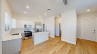 This single-story space showcases a clean, contemporary design defined by light wood-look flooring, crisp white walls, and recessed lighting throughout. The open-concept kitchen and living area serves as the heart of the home, featuring two-tone cabinetry in white and warm gray, bright white quartz countertops, and a central island that provides additional workspace and casual seating. Stainless steel appliances, including a French door refrigerator, electric range, built-in microwave, and dishwasher, complete the well-appointed kitchen. A sliding glass door connects the living area directly to a private outdoor patio, filling the space with natural light and offering easy indoor-outdoor access.

The bedrooms maintain the same consistent aesthetic, each featuring light wood flooring, ceiling fans, and windows with blinds that allow ample natural light. One bedroom includes access to a walk-in closet with built-in storage. The bathroom is finished with light wood-tone cabinetry, a white countertop vanity, a glass-enclosed shower, and a window for natural ventilation. Throughout the entire space, the neutral color palette and modern finishes create a cohesive, bright, and inviting atmosphere.