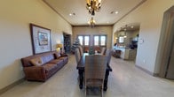 This single-story community facility in Lubbock, Texas offers a welcoming and functional layout designed for group gatherings and activities. The main gathering area is anchored by an elegant dark wood dining table with upholstered seating for eight, illuminated by decorative wrought-iron chandeliers that hang from the elevated tray ceiling. Polished concrete floors flow throughout, lending the space a clean, durable aesthetic. A comfortable seating area with a leather sofa provides a relaxed lounge space alongside doors that let in abundant natural light. Adjacent to the main room, the fully equipped galley-style kitchen features dark granite countertops, a double sink, pendant lighting, dark cabinetry, and a water cooler station, making it well-suited for catering and event preparation. A dedicated recreation room offers generous open floor space with an air hockey table, a foosball table, built-in shelving stocked with books and games, and small-group seating — ideal for children and youth programming. Natural light enters through multiple windows fitted with blinds. The overall design blends warm earth tones with practical finishes, creating an inviting atmosphere suitable for community events, meetings, and recreational programming throughout the year.