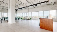 Located on an upper floor of 855 Main St in downtown Bridgeport, Connecticut, this generously sized amenity space offers a sophisticated blend of industrial architecture and modern design. Exposed concrete ceilings with visible ductwork and structural beams lend an authentic loft character, while large floor-to-ceiling windows wrap around the perimeter, flooding the interior with abundant natural light and framing sweeping panoramic views of the Bridgeport skyline and surrounding cityscape.

The main open-plan area is finished with large-format light stone tile flooring and features distinct lounge and dining zones. Comfortable seating clusters with cream and green upholstered sofas invite relaxed gatherings, while dining tables paired with teal and cream chairs with gold-accented legs provide a polished setting for more structured use. A warm wood-topped bar counter adds a welcoming focal point.

A dedicated game room houses a billiards table set against bright white walls and natural light. A pet grooming station with a stainless steel tub and grooming table offers a practical convenience. The space connects directly to an expansive rooftop deck, outfitted with teak-framed outdoor furniture and offering unobstructed 360-degree views of Bridgeport and beyond. A full bathroom completes the floor.