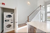 Located at 260 Avenue E in Bayonne, NJ, this modern two-story residence offers a thoughtfully designed layout spread across two floors. The main level features an open-concept living, dining, and kitchen area with soaring ceilings that flood the space with natural light. The kitchen is a standout, boasting bold cobalt-blue upper cabinetry, dark wood lower cabinets, a subway tile backsplash, stainless steel appliances, and a generous quartz-topped island with an undermount sink — ideal for both cooking and entertaining. Wide-plank hardwood flooring runs throughout, complementing the clean white walls and modern aesthetic. A dedicated laundry area and multiple closets add practical convenience. The upper loft level offers additional flexible living space and leads to a private balcony enclosed by sleek glass railings, where panoramic views of the Bayonne skyline and distant waterway create a striking backdrop. The primary bedroom is well-proportioned and benefits from large windows that frame the same sweeping cityscape. Three bathrooms are finished with marble-look tile flooring and white subway tile; one features a soaking tub, while another offers a frameless glass walk-in shower and contemporary wood-toned vanity. A staircase with cable railings connects both levels with open, airy elegance.