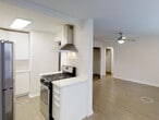 Located at 1001 Sherman Street in Denver, Colorado, this single-floor residence offers a clean, modern aesthetic with a thoughtfully designed open layout. The kitchen is equipped with a stainless steel gas range and a sleek stainless steel wall-mounted range hood, complemented by white cabinetry and a bright white countertop. A half-wall divider separates the kitchen from the living area, maintaining an open and connected feel while providing subtle spatial definition. The living area features smooth, light-toned hardwood-style flooring that extends throughout the space, contributing to a cohesive and airy atmosphere. A ceiling fan with a light fixture is centrally positioned in the living area, offering both functionality and a classic touch. Crisp white walls and clean crown molding add a polished finish to the interior. A charming arched doorway leads to what appears to be a closet or additional room, adding an architectural detail that softens the overall design. The space is bright and well-maintained, with a neutral color palette that provides a versatile backdrop suitable for a variety of interior styles.