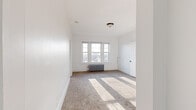 This single-floor unit offers a clean, functional layout with a bright and neutral aesthetic throughout. The living spaces are finished with plush wall-to-wall carpeting and crisp white walls, creating a light and airy atmosphere. Multiple rooms benefit from natural light streaming through gridded double-hung windows, with classic cast-iron radiators positioned beneath several of them, highlighting the unit's period character.

The carpeted bedrooms are generously proportioned, with one featuring a trio of windows that cast broad bands of sunlight across the floor. Closet storage is well-considered, with dedicated closets accessible through paneled white doors. One bedroom includes a double-door configuration offering access to both a closet and an adjoining hallway.

The kitchen is thoughtfully updated, featuring white shaker-style cabinetry, a subway tile backsplash, dark granite-look countertops, a matte black faucet, and light wood-look flooring. A gas range and stainless refrigerator complete the space, alongside a charming glass-panel built-in cabinet that adds vintage character.

The bathroom retains its classic appeal with white subway tile walls accented by bold dark border tiles, a full soaking tub, and a bright window providing natural ventilation and light over wood-look tile flooring.