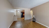 This single-floor, 2-bedroom, 1-bathroom residence offers a practical and well-organized layout across its compact footprint. The living room serves as the central gathering space, featuring warm wood-look laminate flooring, neutral beige walls, and a textured ceiling throughout. A large window with vertical blinds allows natural light to fill the room, creating a bright and welcoming atmosphere, while a front entry door provides direct access to the space.

The kitchen is open to the living and dining area, separated by a partial wall with a pass-through counter. It features rich dark cherry-toned cabinetry, granite-style countertops, black appliances including a full-size refrigerator, and a pendant light overhead, lending the area a cohesive and functional character.

Both bedrooms are carpeted and share a similar neutral palette, each equipped with a window that brings in natural light. The primary bedroom offers a comfortable footprint with adequate closet access nearby.

The full bathroom includes a single-sink vanity with dark cabinetry and stone-style countertop, a toilet, and a shower-tub combination. Wood-look flooring extends into this space, maintaining consistency with the rest of the unit. A hallway connects the bedrooms and bathroom, completing the straightforward and efficient floor plan.