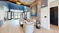 Located in Venice, Florida, this single-story community clubhouse offers a thoughtfully designed gathering space that blends coastal charm with modern sophistication. The welcoming entrance lobby features herringbone wood-panel accent walls, light hardwood flooring, bold navy cabinetry, and a striking pendant light, setting an inviting tone from the moment you step inside. A curated seating area with rounded lounge chairs provides a comfortable spot for casual conversations.

The expansive main lounge is anchored by soaring ceilings with exposed wood beams and shiplap detailing, a dramatic chandelier, and a wall of oversized windows that flood the space with natural light and frame views of the outdoor pool area. A generously sized sectional sofa surrounds a live-edge wood coffee table, creating an ideal setting for relaxation or socializing. A dedicated media nook showcases a bold, artistic tile feature wall in layered blue tones with navy built-in cabinetry below.

A secondary sitting area offers intimate seating around a round marble-top table, bathed in natural light from tall windows. The kitchenette is outfitted with quartz countertops, a stainless steel undermount sink, matte black fixtures, a white subway tile backsplash, and navy open shelving. A fully equipped fitness center with glass door access completes this well-appointed community facility.