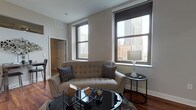 Located at the heart of Cleveland on the historic Public Square, this single-floor residence offers a well-designed layout with an open, flowing floor plan ideal for both comfortable living and entertaining. The living area is a welcoming space anchored by rich hardwood flooring, neutral-toned walls, and large windows that frame impressive views of the Cleveland skyline, flooding the room with natural light and providing a striking urban backdrop. The kitchen is thoughtfully appointed with warm wood cabinetry, dark granite countertops, a tile backsplash, stainless steel appliances, and a breakfast bar with pendant lighting — combining function and style in equal measure. The primary bedroom is generously proportioned, featuring plush carpeting, a walk-in closet area, and an en-suite bathroom with warm wood vanity cabinetry, a gray stone countertop, and light tile flooring. The second bedroom offers its own closet and a similarly calm, neutral aesthetic with carpeted flooring. A second full bathroom mirrors the refined finishes found throughout the home. Exposed structural beams in the bedrooms add an architectural character, while ceiling fans and ample storage enhance everyday functionality. The overall ambiance is modern, polished, and ideally situated for urban living in downtown Cleveland.