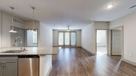 This thoughtfully designed 2-bedroom, 2-bathroom residence is laid out on a single floor, offering a cohesive and functional living experience. The open-concept kitchen and living area serves as the heart of the home, featuring rich hardwood-style flooring that flows throughout the main living spaces. The kitchen is outfitted with granite countertops, a large center island with pendant lighting, stainless steel appliances including a French door refrigerator, and two-tone cabinetry in white and gray. The spacious living room extends toward a set of glass French doors that invite natural light and provide access to the outdoors, complemented by a ceiling fan overhead. The bedrooms are carpeted for comfort, each featuring windows with blinds and ceiling fans. The primary bedroom is a generous size and is accompanied by a well-appointed en-suite bathroom boasting granite vanity countertops, a glass-enclosed shower, and direct access to a large walk-in closet with extensive built-in shelving. A second walk-in closet provides additional storage. The second bathroom mirrors the same quality finishes found throughout the residence. Neutral tones and clean lines give the entire space a modern, move-in-ready ambiance.