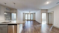 This thoughtfully designed 2-bedroom, 2-bathroom residence is laid out on a single floor, offering a cohesive and functional living experience. The open-concept kitchen and living area serves as the heart of the home, featuring rich hardwood-style flooring that flows throughout the main living spaces. The kitchen is outfitted with granite countertops, a large center island with pendant lighting, stainless steel appliances including a French door refrigerator, and two-tone cabinetry in white and gray. The spacious living room extends toward a set of glass French doors that invite natural light and provide access to the outdoors, complemented by a ceiling fan overhead. The bedrooms are carpeted for comfort, each featuring windows with blinds and ceiling fans. The primary bedroom is a generous size and is accompanied by a well-appointed en-suite bathroom boasting granite vanity countertops, a glass-enclosed shower, and direct access to a large walk-in closet with extensive built-in shelving. A second walk-in closet provides additional storage. The second bathroom mirrors the same quality finishes found throughout the residence. Neutral tones and clean lines give the entire space a modern, move-in-ready ambiance.
