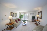 This single-floor unit offers a well-organized layout across several distinct spaces. The living room serves as the central gathering area, finished with plush carpeting, a textured ceiling, and large sliding glass doors fitted with vertical blinds that invite natural light and provide outdoor views. Baseboard heating runs along the perimeter, and the room is generously sized to accommodate comfortable seating arrangements.

The kitchen is designed for functionality, featuring warm oak cabinetry, light countertops, and tile flooring. It is equipped with a full suite of appliances, including an electric range, refrigerator, and dishwasher, with an overhead exhaust hood above the stove.

Adjacent to the kitchen, the dining area offers tile flooring and includes a ceiling fan with a light fixture. An electrical panel is conveniently accessible within this space.

The unit includes two bedrooms, both carpeted and equipped with ceiling fans. Each bedroom features a sliding closet, and windows allow for natural light. One bedroom includes an additional door providing access to a secondary space.

The bathroom is well-appointed with a single-sink vanity featuring oak cabinetry and a light-colored countertop, a large wall mirror with overhead lighting, and a full tub-shower combination.