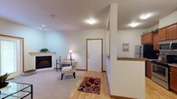 Located at 2505 East Main Street in Puyallup, WA, this single-floor residence offers a well-designed, open layout with a warm and inviting ambiance throughout. The living room is a comfortable centerpiece, featuring plush carpet, large windows that welcome natural light, and a door providing direct outdoor access. A fireplace adds a cozy focal point to an adjacent sitting area near the entry. The dining area is defined by elegant hardwood-style flooring, a chandelier overhead, and ample space for a dining set. The galley kitchen is efficiently arranged with rich wood cabinetry, granite-style countertops, a double sink, and stainless steel appliances including a refrigerator, range, and microwave. The primary bedroom offers a generous window with outdoor views and plush carpeting, creating a restful retreat. A second bedroom, also carpeted and naturally lit, provides flexible use as a guest room or additional living space. The bathroom features tile flooring, a full tub and shower combination, and wood-toned cabinetry. Consistent wood trim accents throughout the unit tie together a cohesive, polished aesthetic, while the open-concept flow between the kitchen, dining, and living areas makes the space feel connected and functional.