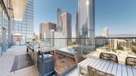 This high-rise rooftop terrace at Park Fifth offers an exceptional outdoor amenity space set against a dramatic downtown skyline backdrop. The expansive terrace is finished with large-format stone pavers and bordered by floor-to-ceiling glass railings that preserve unobstructed, panoramic views of the surrounding urban landscape, including prominent towers and city landmarks in every direction.

A dedicated outdoor kitchen area runs along one side of the terrace, equipped with a full-sized stainless steel barbecue grill, a built-in sink, and counter workspace — designed for resident use in accordance with clearly posted barbecue rules and regulations. Adjacent to the grill station, raised planting beds add a touch of greenery, softening the terrace's contemporary aesthetic with natural landscaping elements.

Throughout the terrace, woven rattan chairs and modern white tables provide comfortable seating arrangements suited for both casual gatherings and relaxed outdoor dining. The space is bordered by a striking glass curtain wall façade with tall, double-door entries, allowing ample natural light to filter through while maintaining a seamless indoor-outdoor connection. The combination of polished architectural details, abundant sunlight, and sweeping cityscape views makes this rooftop terrace a standout communal feature of the building.