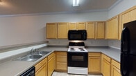 Located at 2792 Stantonsburg Rd in Greenville, NC, this single-floor unit offers a practical and well-organized layout designed for comfortable living. The open-concept living area is finished with wall-to-wall carpeting and crown molding, and flows directly into the kitchen via a breakfast bar-style pass-through, creating a connected and functional common space. The kitchen is well-appointed with light wood cabinetry offering ample upper and lower storage, gray laminate countertops, a double-basin sink, a coil-top electric range, an over-the-range microwave, a dishwasher, and tile flooring. Ceiling fans with integrated lighting fixtures are present in both the living area and bedroom, providing comfortable air circulation. The bedroom features plush carpeting, a window with blinds allowing natural light, and access to a generously sized walk-in closet equipped with wire shelving on multiple levels. The bathroom includes a wide vanity with a single sink, a large mirror with overhead lighting, and tile flooring. A dedicated laundry room provides washer and dryer hookups with overhead wire shelving for additional storage, completing this efficiently designed single-floor space.