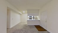 This single-story residence offers a thoughtfully arranged floor plan accommodating six bedrooms and one full bathroom across a generously sized living footprint. The open-concept kitchen and living area serves as the heart of the home, where a peninsula with marble-style countertops connects the two spaces seamlessly. The kitchen is well-equipped with stainless steel appliances, including a range, microwave, and refrigerator, complemented by crisp white cabinetry and wood-style flooring that adds warmth underfoot. The adjacent living area features plush carpeting, a window, and a glass door that invites natural light into the space. Each of the six bedrooms is finished with soft carpet and neutral walls, providing a clean, versatile canvas. The primary bedroom includes a mirrored sliding-door closet with built-in shelving, offering practical storage. The full bathroom is appointed with a marble-style vanity countertop, a large mirror with vanity lighting, wood-style flooring, and a tiled soaking tub and shower combination with decorative tile accents. A ceiling fan in the primary bedroom area adds to the comfort of the space. Overall, the home presents a clean, updated aesthetic with a neutral color palette throughout.