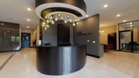 Located at 8 Tice Road in Franklin Lakes, NJ, The Franklin is a polished, single-floor commercial space that exudes contemporary sophistication throughout. The centerpiece of the space is a sweeping, curved reception desk finished in brushed dark metal, positioned beneath a dramatic circular ceiling detail adorned with a cascading cluster of globe pendant lights. The "The Franklin" branding is prominently displayed on a dark feature wall, establishing a strong and professional first impression.

The entrance foyer features large-format white tile flooring accented with contrasting marble inlays, welcoming visitors through glass-paneled doors that flood the space with natural light. Floor-to-ceiling glass partitions with sleek black steel framing enclose dedicated meeting and conference areas, maintaining visual openness while providing functional separation.

A refined lounge area offers plush burgundy velvet seating arranged around a circular black and gold coffee table, beneath a brass sputnik chandelier with wall sconce accents. A dramatic veined marble wall panel serves as an elegant backdrop, lending warmth and texture to the space.

Corridors are lined with rich, dark marble cladding surrounding elevator bays, complemented by recessed lighting and curated floral arrangements. Throughout, the design balances bold contrasts of dark and light, with refined finishes that convey a premium, professional atmosphere.