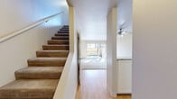 Located at 1450 Creekside Dr in Walnut Creek, CA, this two-story home offers two bedrooms and one bathroom across a well-organized layout. The main floor features warm hardwood flooring throughout the living and kitchen areas. The kitchen is designed with white cabinetry, light stone countertops, and a peninsula that opens to the main living space, creating a functional and connected flow. The living room is bright and airy, highlighted by a ceiling fan, large windows, and a sliding glass door that opens to a private outdoor patio area. Carpeted stairs lead to the upper floor, where both bedrooms are located. The primary bedroom is a comfortable size and features a closet with built-in shelving, carpeted flooring, and a window with outdoor tree views. The second bedroom is similarly carpeted and bathed in natural light from a large window. A full bathroom on the upper floor includes a shower-tub combination with grab bars and clean white tile. Each bedroom benefits from dedicated closet space, and a hallway connects the upper-level rooms. The overall aesthetic is clean and neutral throughout, with light-toned walls and an abundance of natural light creating a welcoming ambiance across both floors.