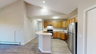 Located at 5771 Chapel Valley Rd in Fitchburg, Wisconsin, this one-bedroom, one-bathroom residence offers a well-designed single-floor layout with a range of thoughtful features throughout. Light-toned luxury vinyl plank flooring runs continuously across the entire space, complementing the neutral, warm-toned walls for a clean and cohesive aesthetic.

The open-concept living area is a standout, featuring soaring vaulted ceilings that amplify the sense of space and a sliding glass door that leads to a private balcony overlooking the well-maintained community grounds. Natural light fills the room, enhancing its airy feel.

The kitchen is efficiently laid out with warm wood cabinetry, light countertops, stainless steel appliances including a refrigerator, dishwasher, and range, and a peninsula that provides additional prep and dining space.

The bedroom offers comfortable proportions, a ceiling fan, a large window with natural light, and a built-in closet with bi-fold doors for ample storage. A baseboard heating system is present throughout the unit.

The bathroom features warm wood vanity cabinetry, a mirror, and a full tub-shower combination with accessibility grab bars, all finished with matching LVP flooring. The balcony provides views of the brick-exterior multi-story buildings and lush green surroundings of the community.