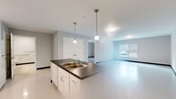 Located at 908 Hartford Tpke in Waterford, Connecticut, this single-floor unit offers a clean, modern layout designed for both comfort and functionality. The open-concept kitchen serves as the heart of the space, featuring white shaker-style cabinetry, dark countertops, white appliances including a range, refrigerator, and microwave, and a central island with a double-basin sink illuminated by pendant lighting overhead. The kitchen flows seamlessly into a generously sized living area finished with light-toned flooring and neutral walls, allowing ample natural light to enter through large windows with outdoor views.

The unit includes multiple rooms with carpeted flooring, well-suited for use as bedrooms or flexible living spaces. Each room benefits from natural light and a clean, understated aesthetic with dark baseboard accents against light walls. A dedicated laundry room houses a full-size Whirlpool front-load washer and dryer with built-in shelving overhead. The bathroom is thoughtfully designed with accessibility in mind, featuring grab bars near the toilet and bathtub, a dark-countered vanity, and a bright, easy-to-clean finish throughout. A wall-mounted mini-split HVAC unit provides climate control. The overall ambiance is bright, functional, and move-in ready.
