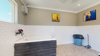 This purpose-built pet grooming room is thoughtfully designed to provide a clean, functional, and comfortable environment for pet care. The room is defined by its classic white subway tile wainscoting that lines all walls to mid-height, paired with warm taupe-painted walls above, creating a clean and hygienic aesthetic throughout. The floor is covered in small-format mosaic tiles, offering both durability and easy maintenance — ideal for a wet-use environment.

The centerpiece of the space is a deep, built-in dog wash tub with a dark wood-paneled exterior surround, equipped with wall-mounted plumbing fixtures and a handheld sprayer for convenient bathing. A professional-grade standing pet dryer on a wheeled stand provides grooming flexibility and easy repositioning throughout the room.

Natural light fills the space through multiple windows, offering pleasant views of lush greenery outdoors. A dedicated exterior entry door provides direct access to the room, adding practical convenience for pet owners. Recessed lighting and a wall-mounted HVAC unit ensure year-round comfort. Crown molding at the ceiling line adds a refined architectural touch. Framed pet-themed artwork adorns the upper walls, lending a welcoming and lighthearted character to this well-appointed grooming space.
