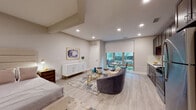 Located at 59 2nd Ave in Raritan, NJ, this thoughtfully designed single-floor residence offers a seamless blend of modern aesthetics and functional living. The open-concept layout connects the living, dining, and sleeping areas, creating an airy and cohesive environment throughout.

The living area is anchored by light hardwood-style flooring, recessed lighting, and a large window with a roller shade that floods the space with natural light and provides views of the surrounding greenery. A plush seating arrangement, glass coffee table, and elegant white sideboard with gold accents add refined character to the room.

The sleeping area is generously proportioned, featuring a full-sized bed with an upholstered headboard, a bedside chest, and ample closet space. The room maintains the same warm, neutral palette found throughout the residence.

The kitchen is well-appointed with rich dark cabinetry, stainless steel appliances including a gas range, microwave, refrigerator, and dishwasher, and clean white countertops. A window adjacent to the kitchen allows for additional natural light.

The bathroom features a full tub-shower combination with mosaic tile surround, a dark wood vanity with a white basin, a large mirror, and neutral tile flooring, completing this polished and practical space.