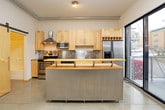 This single-floor unit showcases a thoughtfully designed industrial-modern aesthetic throughout. The open-plan living area is anchored by large floor-to-ceiling windows that flood the space with natural light and offer views of the surrounding streetscape. Exposed ductwork runs along the ceilings, complementing the polished concrete and large-format tile flooring found throughout the unit. Ceiling fans are installed in key living areas, enhancing both comfort and style.

The kitchen is a standout feature, outfitted with light maple cabinetry, stainless steel appliances including an electric range, microwave, dishwasher, and refrigerator, along with a stainless steel backsplash and a butcher block breakfast bar. A sliding glass door connects the kitchen directly to an outdoor balcony, providing convenient access to fresh air and exterior views.

The bedrooms are well-proportioned, each featuring large-panel sliding closets in light wood tones and ceiling fans. The unit includes two bathrooms: one with a tiled shower-tub combo, rich dark wood vanity, and large-format tile flooring, and a second more utilitarian bathroom with a soaking tub, toilet, and polished concrete flooring. A barn-style sliding door adds a distinctive architectural touch to one of the bedroom entries.