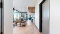 Located on Peachtree Street in Atlanta's Midtown neighborhood, this sophisticated amenity lounge at Loria Atlanta offers a well-appointed, single-floor space designed for both socializing and relaxation. The open-concept layout flows seamlessly from a welcoming reception area — highlighted by a warm wood-paneled ceiling, a central white island with bar seating, and distinctive textured accent walls — into the main living and dining areas.

The living room is bathed in natural light through floor-to-ceiling glass walls that frame panoramic views of the Atlanta skyline and surrounding treetops. Mid-century modern furnishings, including a rich leather sofa, wooden armchairs, and layered area rugs, create an inviting and stylish atmosphere. A suspended mesh screen partition adds an architectural touch while subtly defining zones within the open space.

The dining room features a substantial wood table surrounded by teal plaid chairs, illuminated by a striking brass-and-bulb chandelier. A built-in wet bar with wine refrigeration and bold geometric wallcovering elevates the room's design character. Floor-to-ceiling windows continue the connection to the city views.

A game room with a billiards table, herringbone carpet, and the Loria-branded display wall rounds out the interior. An adjacent outdoor terrace, enclosed by glass railings, offers unobstructed elevated views of Atlanta's skyline and greenery.