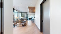 Located on Peachtree Street in Atlanta's Midtown neighborhood, this sophisticated amenity lounge at Loria Atlanta offers a well-appointed, single-floor space designed for both socializing and relaxation. The open-concept layout flows seamlessly from a welcoming reception area — highlighted by a warm wood-paneled ceiling, a central white island with bar seating, and distinctive textured accent walls — into the main living and dining areas.

The living room is bathed in natural light through floor-to-ceiling glass walls that frame panoramic views of the Atlanta skyline and surrounding treetops. Mid-century modern furnishings, including a rich leather sofa, wooden armchairs, and layered area rugs, create an inviting and stylish atmosphere. A suspended mesh screen partition adds an architectural touch while subtly defining zones within the open space.

The dining room features a substantial wood table surrounded by teal plaid chairs, illuminated by a striking brass-and-bulb chandelier. A built-in wet bar with wine refrigeration and bold geometric wallcovering elevates the room's design character. Floor-to-ceiling windows continue the connection to the city views.

A game room with a billiards table, herringbone carpet, and the Loria-branded display wall rounds out the interior. An adjacent outdoor terrace, enclosed by glass railings, offers unobstructed elevated views of Atlanta's skyline and greenery.