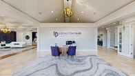 The Lexington Park Apartment Homes clubhouse in North Little Rock, Arkansas offers a thoughtfully designed community space that blends sophistication with functionality. The welcoming entry lobby features soaring vaulted ceilings, a dramatic orb chandelier, large French doors flooding the space with natural light, and a stylish reception desk set against a textured accent wall — all anchored by a striking marble-patterned area rug.

The main living area impresses with an elaborate coffered ceiling, a second orb pendant light, a fireplace with a mounted TV, and a built-in seating nook framed by deep navy accent walls. Crisp white sofas, gold-accented furnishings, and rich hardwood floors create an upscale yet inviting atmosphere throughout.

A dedicated workstation area features a long communal desk set against a stacked-stone accent wall, offering residents a quiet space for productivity. The game room, bathed in natural light from multiple windows, includes a full-size pool table on warm hardwood floors, casual seating, and a ceiling fan — ideal for recreation and socializing.

A connecting hallway, accented with crown molding and hardwood floors, ties the spaces together seamlessly. The facility also includes a well-appointed full bathroom with tile flooring, a walk-in shower, and clean white cabinetry for resident convenience.