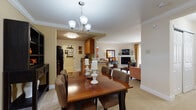 This single-floor residence offers a thoughtfully designed open layout that seamlessly connects the main living areas. The dining area serves as a central hub, featuring crown molding, a chandelier overhead, and direct sightlines into both the kitchen and the living room. A large hutch provides display and storage space, adding a classic touch to the dining experience.

The galley-style kitchen is well-equipped with warm wood cabinetry, dark granite countertops, tile flooring, and black appliances including a range, refrigerator, microwave, and dishwasher. Ample upper and lower cabinetry ensures generous storage throughout.

The living room is anchored by a fireplace and opens to natural light through a draped window, creating a comfortable and inviting atmosphere. Neutral carpet flooring extends through the main living spaces and into both bedrooms.

The primary bedroom features a bold terracotta accent wall, walk-in closet access, and a warm, intimate ambiance. The second bedroom offers a cooler gray palette with carpeted flooring. Both bathrooms include tile flooring and tub-shower combinations, with the full bath featuring wood vanity cabinetry and stone-tiled surround.