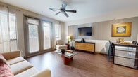 Located at 1255 N Post Oak Rd in Houston, TX, this thoughtfully designed one-bedroom, one-bathroom residence offers a comfortable and stylish living experience across a single floor. The open-concept living and dining area is anchored by warm hardwood-style flooring, a ceiling fan, and large windows with blinds that invite an abundance of natural light. A decorative accent wall provides an elegant focal point for the living space, complementing the room's modern, cohesive aesthetic. The kitchen is a standout feature, boasting rich dark cabinetry, granite-style countertops, a breakfast bar with seating for three, pendant lighting, and a full suite of black appliances, including a refrigerator with ice maker, range, and built-in microwave. The bedroom offers a serene retreat with plush carpet flooring, a striking gold-striped accent wall, large windows with views of greenery, and two generous closets fitted with wire shelving for ample storage. The bathroom features tile flooring, dark wood cabinetry for additional storage, and a framed mirror. Throughout the residence, a warm, neutral color palette and consistent design details create a cohesive and inviting ambiance.