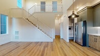Located in Bozeman, MT, this thoughtfully designed two-story home offers three bedrooms and three bathrooms across a well-proportioned layout. The main floor makes an immediate impression with soaring double-height ceilings, warm hardwood-style flooring, and a striking open staircase with white railings that connects to an airy upper-level overlook. The kitchen is a standout feature, outfitted with two-tone cabinetry—dark upper cabinets paired with natural wood lowers—white quartz countertops, a classic subway tile backsplash, stainless steel appliances, and a window above the sink that fills the space with natural light. Built-in shelving adds functional storage on the main level. Upstairs, the bedrooms are carpeted and bright, with large windows offering neighborhood views and recessed lighting overhead. The primary bedroom includes direct access to a dedicated bathroom and a walk-in closet. The bathrooms are finished to a high standard, featuring warm wood vanities with white quartz counters, black-framed mirrors, sleek hardware, and large-format tile flooring. One bathroom showcases a soaking tub with full-height marble-look tile surround. Clean lines, neutral tones, and quality materials define the overall aesthetic of this modern Bozeman home.