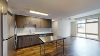 Located at 100 Commons Park N in Stamford, Connecticut, this single-floor unit offers a contemporary, well-appointed living space defined by rich hardwood flooring that flows throughout. The kitchen is a standout feature, outfitted with wood-grain cabinetry, white quartz countertops, and a full suite of stainless steel appliances including a gas range, microwave, refrigerator, and dishwasher. A stainless steel prep table adds a functional, industrial touch to the culinary space, which is illuminated by a recessed panel light fixture above.

The living areas are bright and open, with clean white walls and generous room proportions that allow for flexible furnishing arrangements. Large floor-to-ceiling windows in multiple rooms flood the interior with natural light and frame views of the surrounding Stamford streetscape, including greenery and the urban skyline. The bedroom features the same warm hardwood flooring and ample wall space, complemented by expansive windows that enhance the sense of openness.

The bathroom is finished with white subway tile surrounding a soaking tub and shower combination, neutral-toned walls, and durable flooring, providing a clean and functional design. Overall, the unit presents a modern aesthetic with quality finishes throughout.