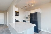 Located at 1201 S Courthouse Rd in Arlington, VA, this one-bedroom, one-bathroom unit offers a thoughtfully organized layout across a single floor. The living and dining area is carpeted in neutral tones and bathed in natural light from a wide bank of windows, creating a bright and open atmosphere. A built-in baseboard heating unit runs along the window wall, ensuring year-round comfort.

The kitchen is efficiently designed with white shaker-style cabinetry, speckled quartz countertops, and a peninsula that doubles as a dining or prep surface. Black appliances — including a gas range, over-the-range microwave, dishwasher, and refrigerator — are complemented by track lighting overhead, lending a modern touch to the space.

The generously sized bedroom features soft carpet flooring, neutral wall tones, and large windows that provide ample natural light. A full-width closet offers substantial storage, and an additional closet is accessible through the bedroom, adding further organizational convenience.

The bathroom is clean and functional, featuring a full tub-shower combo with white tile surround, a toilet, and a vanity with mirror storage. The overall palette throughout the unit is light and neutral, giving the space a fresh, move-in-ready feel.