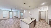 Located in Tomball, Texas, this single-story 2-bedroom, 3-bathroom residence offers a well-designed open-concept layout with modern finishes throughout. The kitchen serves as the centerpiece of the living area, anchored by a large granite-topped island with an undermount sink and a professional-style pull-down faucet, illuminated by elegant pendant lighting. Dark espresso cabinetry contrasts beautifully with the light granite countertops, while stainless steel appliances — including a refrigerator, range, and microwave — complete the space. White subway tile backsplash adds a clean, contemporary touch. The kitchen flows seamlessly into the living room, which features warm wood-look luxury vinyl flooring, a ceiling fan, and a glass door that invites natural light. Both bedrooms are carpeted and feature ceiling fans, windows with blinds, and generous closet space. The three bathrooms are finished with matching dark cabinetry, granite vanities, and wood-look flooring. One bathroom includes a glass-enclosed walk-in shower with white subway tile, while another offers a full soaking tub with a tiled surround. A dedicated laundry room with built-in shelving adds everyday convenience, rounding out this thoughtfully appointed home.
