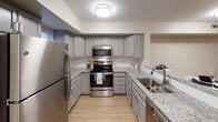 Located at 11 Winthrop St in Rochester, NY, this two-floor residence offers a thoughtfully designed interior with modern finishes throughout. The kitchen serves as a functional centerpiece, featuring gray shaker-style cabinetry, granite countertops, and a full suite of stainless steel appliances, including a refrigerator, electric range with microwave above, and a deep undermount sink. Light wood-style flooring runs through the kitchen, which also includes a peninsula that provides additional counter space and open sight lines into the adjoining living area. The open layout of the main level is reinforced by neutral wall tones and flush ceiling lighting. Bedroom spaces are carpeted and finished with warm neutral walls, with at least one room featuring a large window that allows natural light and exterior views. Closet access is present in the bedrooms, adding practical storage. The bathrooms are clean and understated, with one offering a tub-shower combination with a curved curtain rod, tile surround, and patterned tile flooring, while another presents a vanity with a light countertop and brushed nickel fixtures. Overall, the space maintains a consistent, contemporary aesthetic across both floors, with durable finishes suited for everyday living.