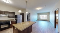 Located in Arden Hills, Minnesota, this well-appointed 2-bedroom, 2-bathroom single-floor residence offers a thoughtfully designed layout with modern finishes throughout. The open-concept kitchen serves as the heart of the home, showcasing rich dark cabinetry, granite countertops, a large central island with pendant lighting, and a full suite of stainless steel appliances including a refrigerator, gas range, dishwasher, and microwave. The kitchen flows seamlessly into a bright and spacious living room, where large windows invite natural light and offer views of the surrounding wooded landscape. Durable hardwood-style flooring runs throughout the entire space, providing a cohesive and easy-to-maintain aesthetic. The generously sized primary bedroom features a ceiling fan and access to a dedicated walk-in closet outfitted with wire shelving for ample storage. Both bedrooms include wall-mounted climate control units and baseboard heating for year-round comfort. The bathrooms are finished with clean, neutral tiling and full bathtub-shower combinations. A dedicated in-unit laundry room houses a full-size front-loading washer and dryer with additional shelving above. The space combines functional design with comfortable living in a convenient Arden Hills location.