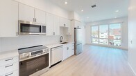 Located at 20 Medford St in Somerville, MA, this thoughtfully designed one-bedroom, one-bathroom residence offers a bright and modern living experience across a single floor. The open-concept layout seamlessly connects the kitchen, dining, and living areas into one cohesive space, bathed in natural light from large floor-to-ceiling windows that frame views of the surrounding Somerville neighborhood. Light-toned hardwood flooring flows throughout, complementing the clean, white interior palette.

The kitchen is outfitted with sleek white cabinetry, quartz countertops, stainless steel appliances including a refrigerator, electric range, dishwasher, and built-in microwave, along with a matte black gooseneck faucet and undermount sink — all lending a contemporary, high-end feel. Recessed lighting illuminates the space efficiently.

The bedroom is a well-proportioned retreat featuring a double-door closet, a window with city views, and the same light hardwood flooring. The bathroom is finished with a subway-tile tub and shower surround in a chevron pattern, accented by sleek matte black fixtures.

Additional highlights include three closets for ample storage, a private balcony with neighborhood views, and in-unit laundry. The overall ambiance is clean, minimal, and modern — ideal for urban living in one of Somerville's vibrant neighborhoods.