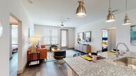 This single-floor residence is thoughtfully designed with a modern aesthetic and functional layout. The open-concept kitchen flows seamlessly into the living area, creating a bright, cohesive space well-suited for both daily living and entertaining. The kitchen is equipped with stainless steel appliances, including a refrigerator, range, and microwave, complemented by light gray cabinetry, a herringbone-patterned tile backsplash, and granite countertops that extend to a peninsula with pendant lighting overhead. Wood-look flooring runs throughout, adding warmth and continuity across all areas.

The living room receives natural light through multiple windows fitted with blinds and features a ceiling fan. A hallway connects the main living spaces to the private areas of the residence, with doors providing separation and storage access along the way.

The bedroom is a comfortable retreat, offering natural light from a window and direct access to a well-organized walk-in closet with built-in shelving and hanging rods on multiple levels. The bathroom features a granite-topped vanity with gray cabinetry, matching the kitchen's design language, and wood-look tile flooring. Overall, the space presents a cohesive, contemporary design with consistent finishes throughout.